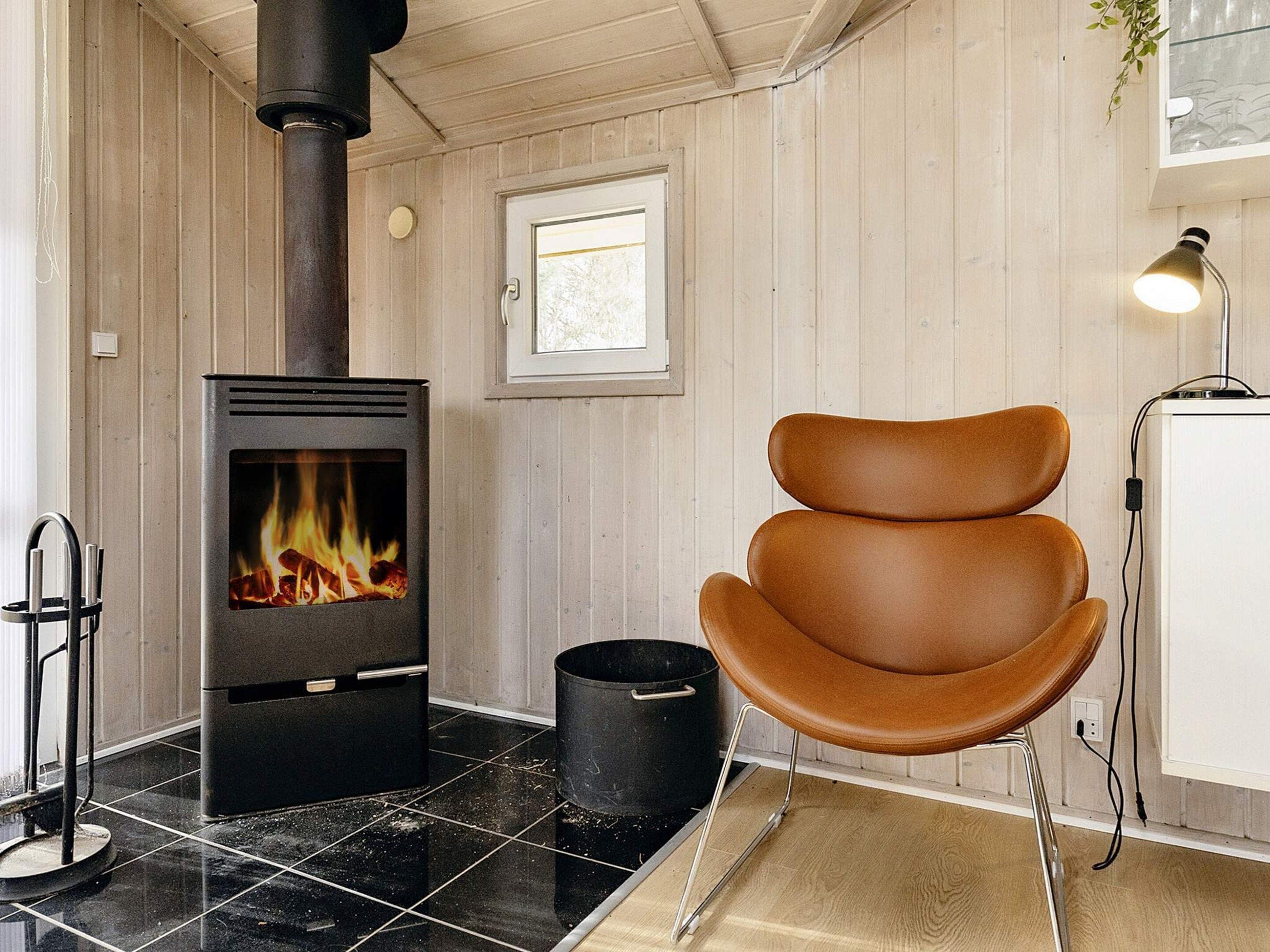 A room with a wood-burning stove, a chair, a window, and a lamp.