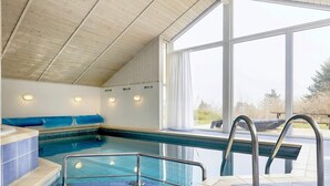 An indoor swimming pool with a blue tiled floor, a bench, and a view of the outdoors through large windows. - 10 Person Holiday Home in Rudkobing (Rudkobing)