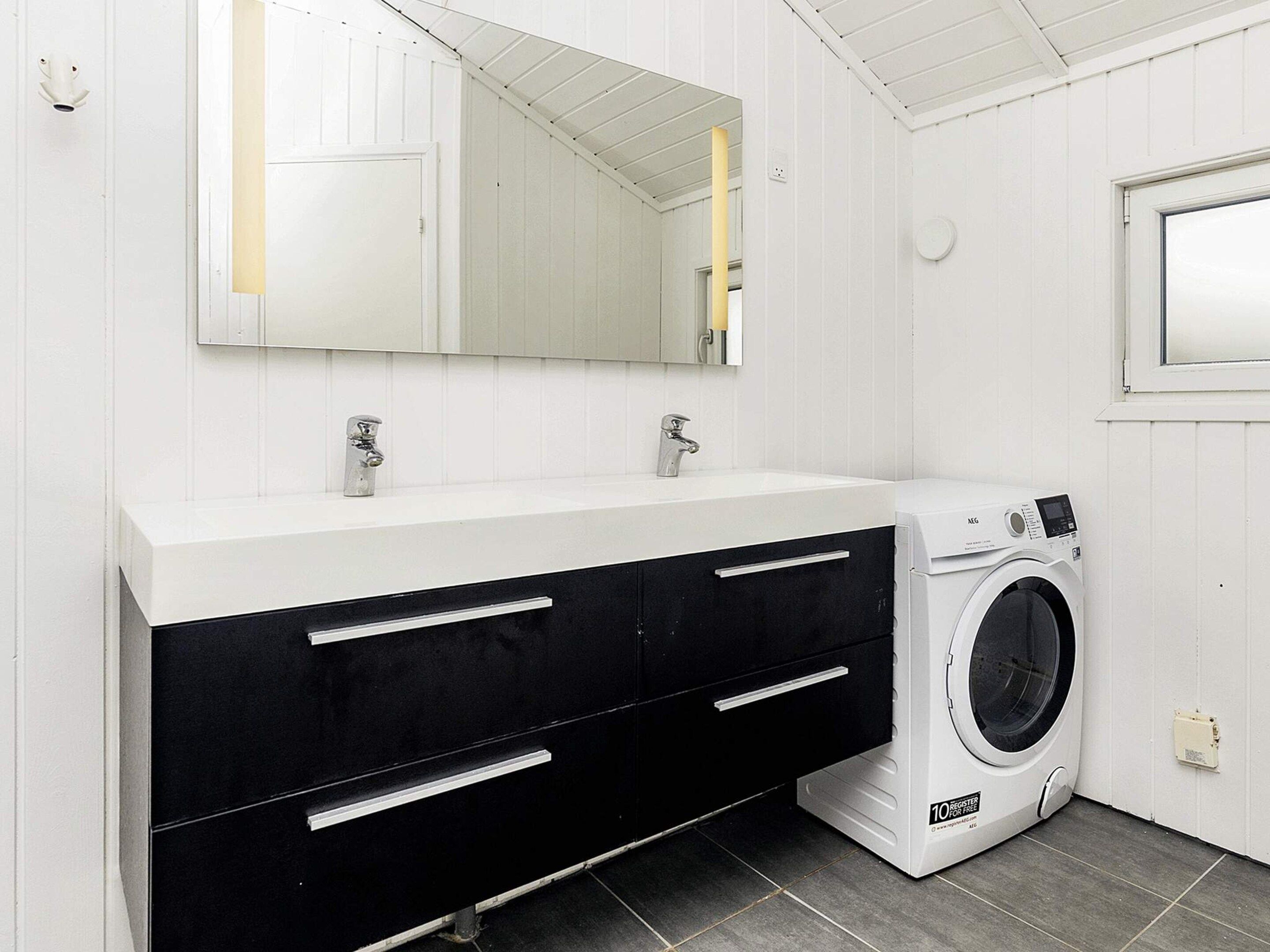 A bathroom with a white vanity, two sinks, a mirror, a washing machine, and a window.
