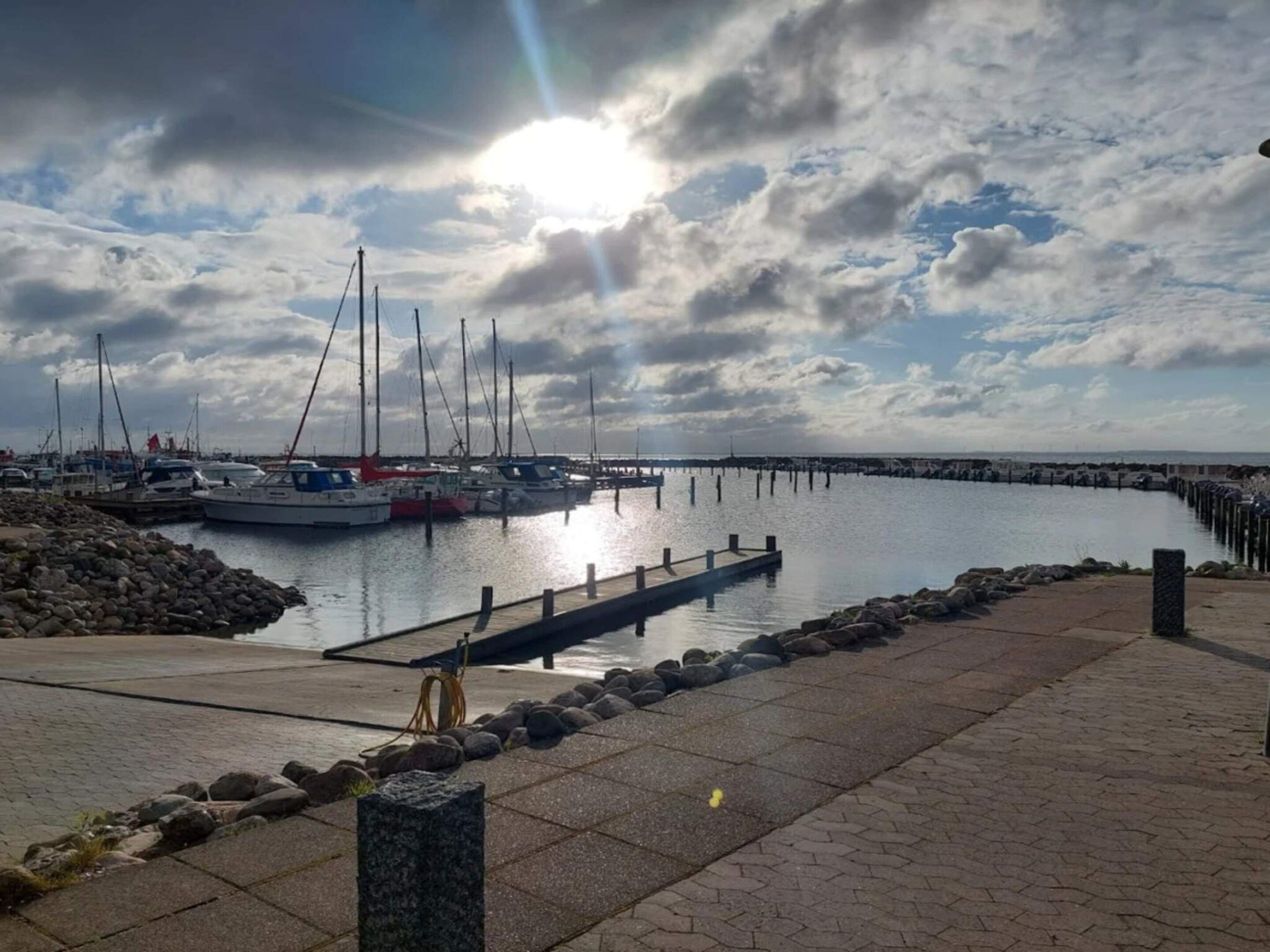 A marina with boats docked, a pier extending into calm water, and a cloudy sky.