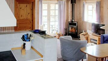 A cozy cabin interior with a kitchen area, a dining table, a sofa, and a wood-burning stove.