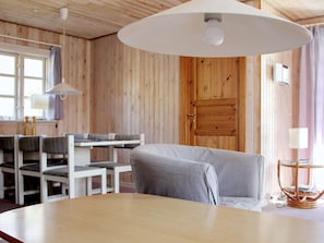 Une pièce chaleureuse avec un décor intérieur en bois, une table ronde, un canapé gris et une fenêtre avec des rideaux.