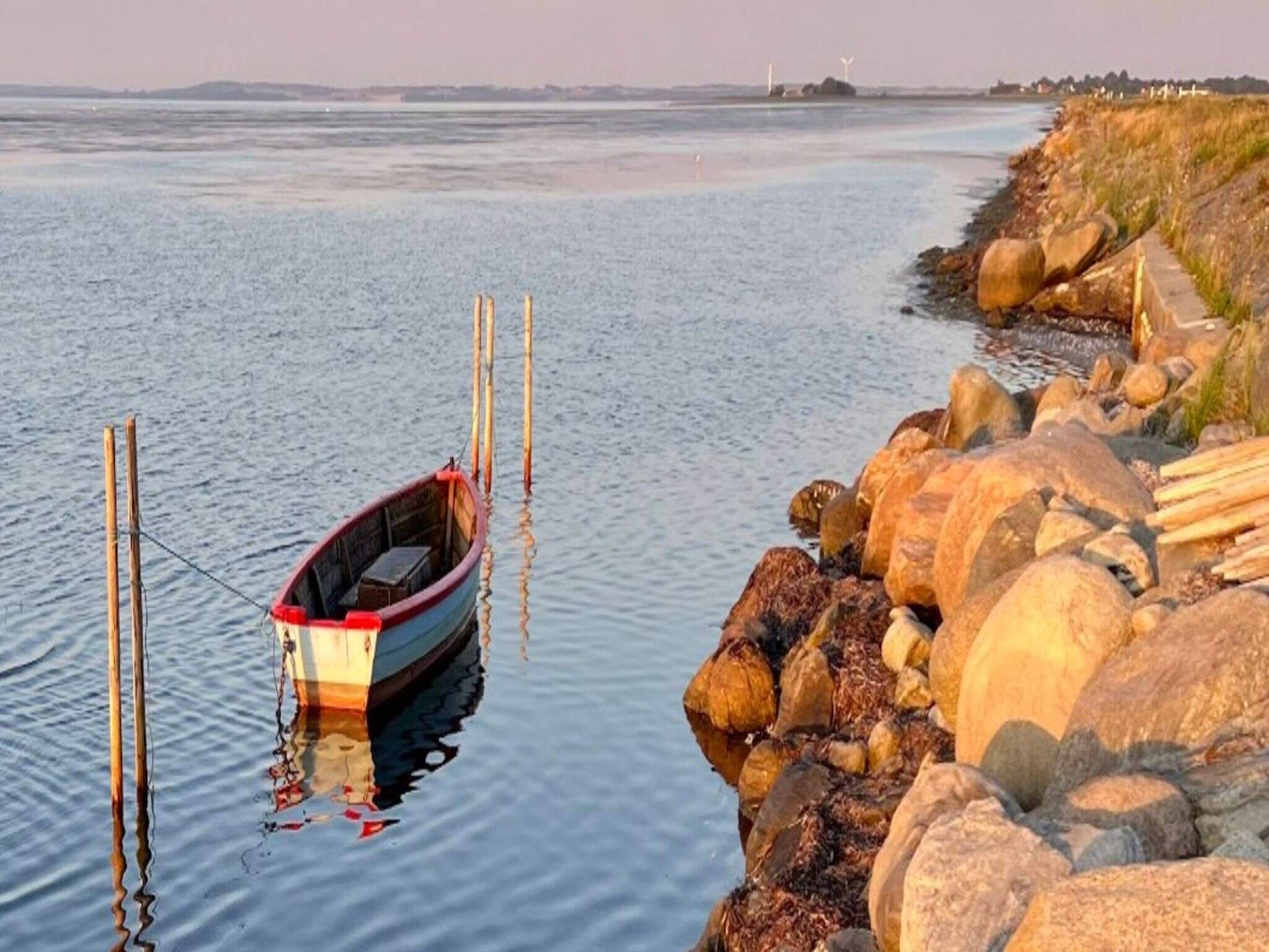 A small boat tied to a wooden dock with a rocky shoreline in the background.