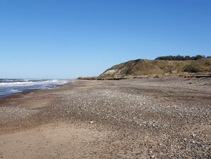 A pebbly beach with a clear sky and a hill in the background. - 6 Person Holiday Home in Brovst (Brovst)