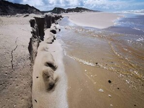 A beach with a narrow strip of sand leading to the water, surrounded by rocky terrain.