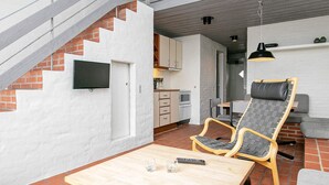 Ein modernes Interieur mit einer Treppe, einer Essecke mit Tisch und Stühlen, einer Küche und einer Wohnbereiches mit Sofa und Sessel.