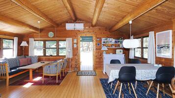 A wooden cabin interior with a dining area, a sofa, and a kitchen.