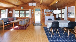 A cozy cabin interior with a wooden ceiling, a dining area with a table and chairs, a sofa, and a small kitchen area with a radio and decorative items. - 4 Person Holiday Home in Sjaellands Odde (Sjællands Odde)