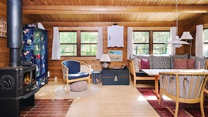 A cozy cabin interior with a wood-burning stove, a sofa, a dining table, and a cabinet with floral patterns. - 4 Person Holiday Home in Sjaellands Odde (Sjællands Odde)