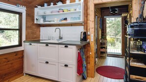 A wooden cabin interior with a kitchen area featuring a sink, cabinets, and a shelf with dishes. - 4 Person Holiday Home in Sjaellands Odde (Sjællands Odde)