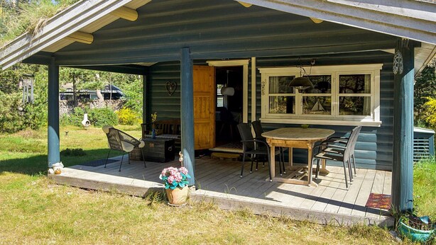 A covered porch with a table and chairs, a window with curtains, and a heart-shaped decoration on the wall. - 4 Person Holiday Home in Sjaellands Odde (Sjællands Odde)