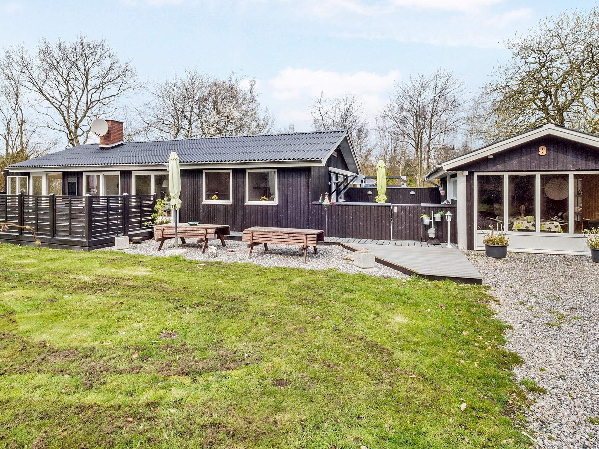 Ein modernes Haus mit einer Terrasse, Sitzgelegenheiten im Freien und einem umzäunten Garten.