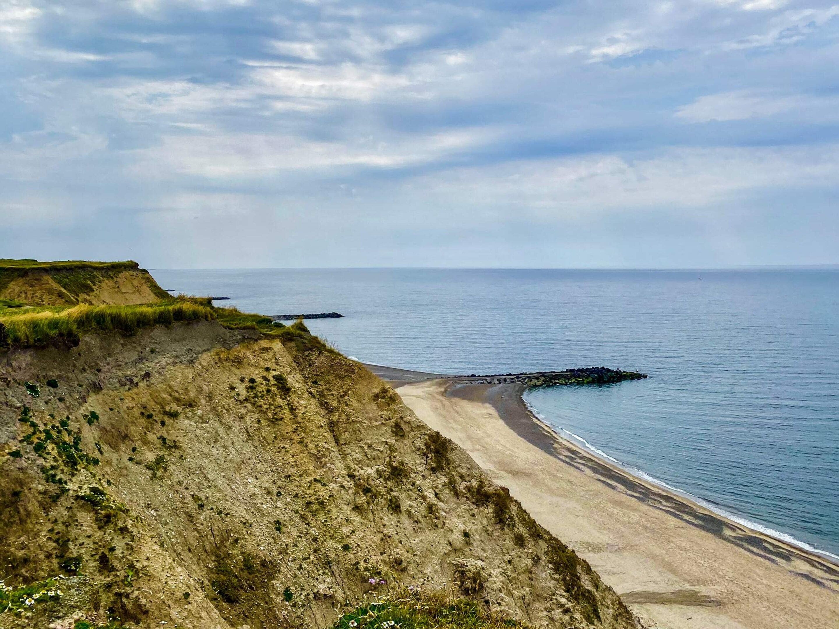 Un paysage côtier avec une plage de sable, des falaises herbeuses et une mer calme.