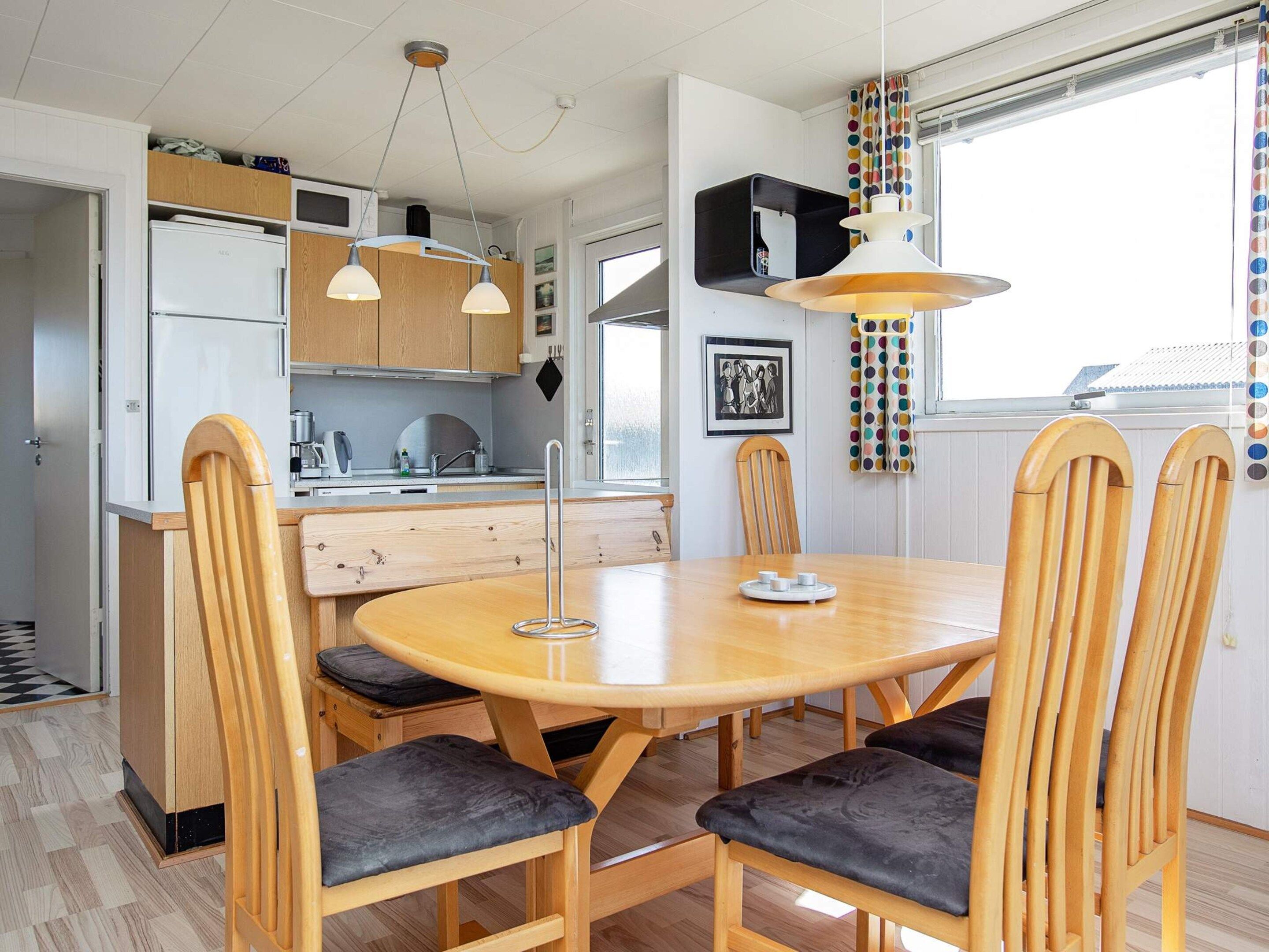 A modern kitchen with wooden cabinets, a dining table with chairs, and pendant lighting.