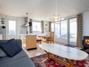 A modern living space with a sofa, dining table, and chairs, a kitchen area, and a fireplace. - 6 Person Holiday Home in Lemvig (Lemvig)