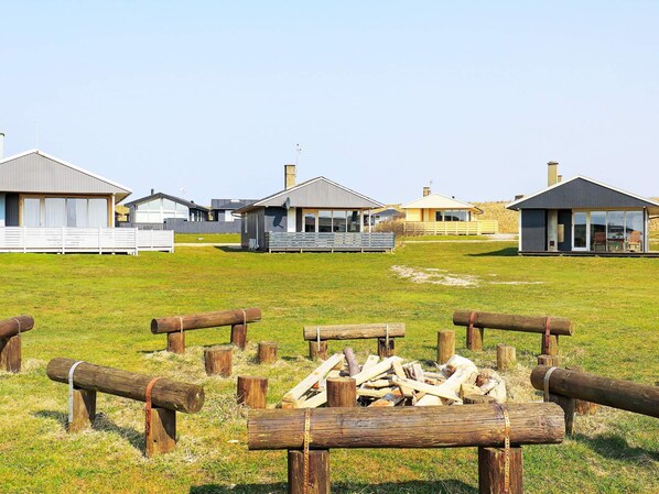 A campground with multiple cabins, a grassy field, and a pile of firewood. - 6 Person Holiday Home in Lemvig (Lemvig)