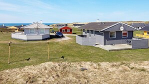 A row of modern, single-story cabins with flat roofs, a car parked in front, and a clear view of the sea in the background. - 6 Person Holiday Home in Lemvig (Lemvig)