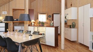 A modern kitchen with wooden cabinets, a dining table with chairs, and a refrigerator. - 4 Star Holiday Home in Hadsund (Hadsund)