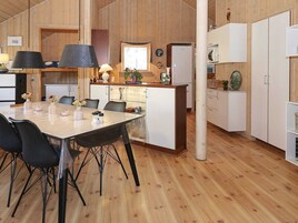 A modern kitchen with wooden cabinets, a dining table with chairs, and a refrigerator.
