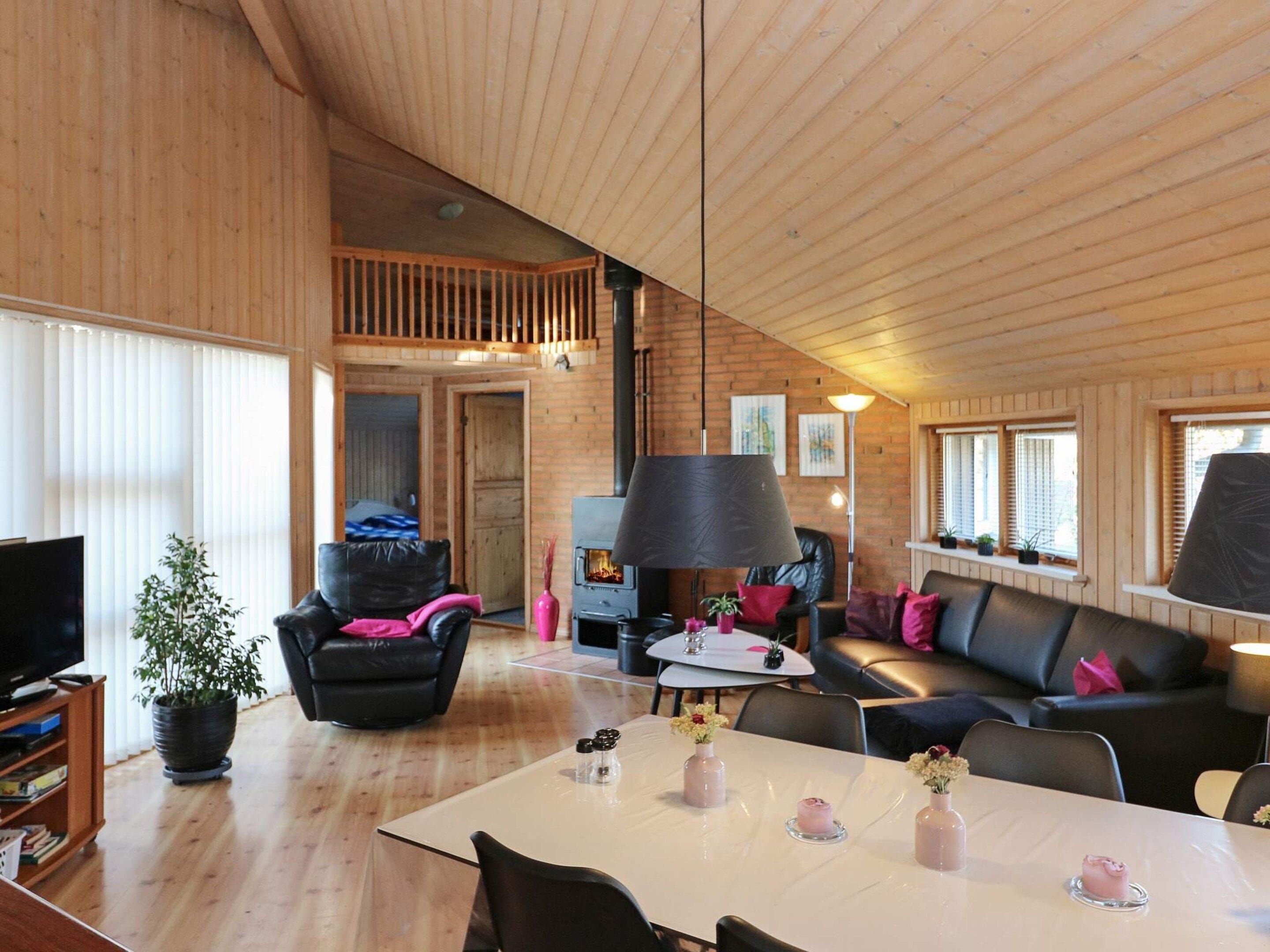 A spacious living area with a high ceiling, wooden walls, a fireplace, a dining table with chairs, and a sofa.