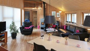 A spacious living area with a high ceiling, wooden walls, a fireplace, and a dining table set with pink vases. - 4 Star Holiday Home in Hadsund (Hadsund)