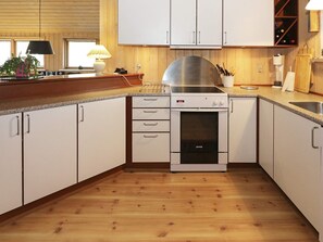 A kitchen with white cabinets, a stainless steel range hood, a built-in oven, and a wooden floor. - 4 Star Holiday Home in Hadsund (Hadsund)