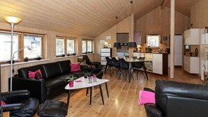 A spacious living area with a wooden floor, black leather sofas, a dining table, and a kitchen in the background. - 4 Star Holiday Home in Hadsund (Hadsund)
