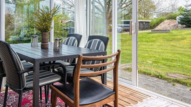 Un invernadero con una mesa y sillas para comer, grandes puertas de cristal y vistas a un jardín con césped.