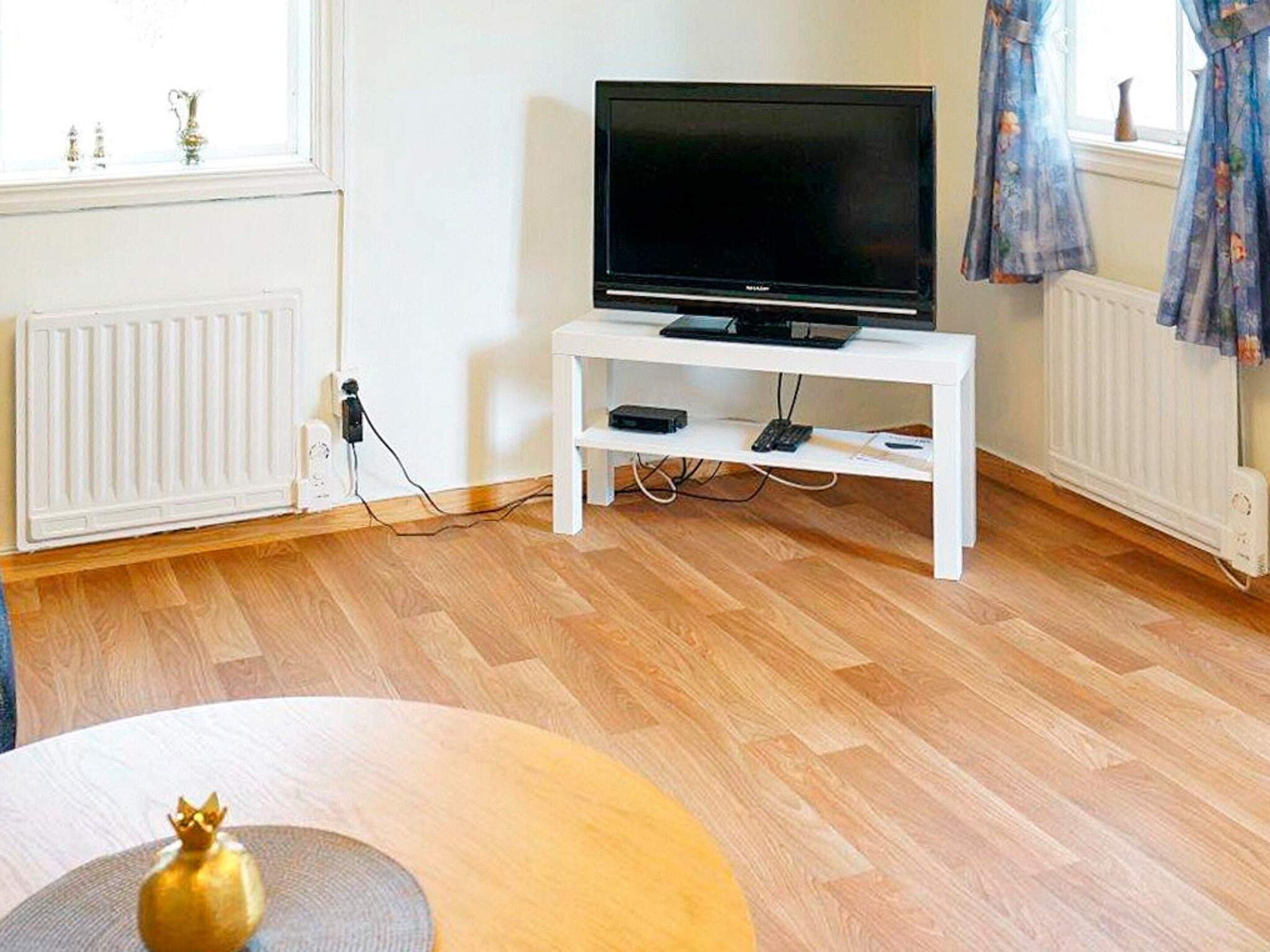 Ein Zimmer mit einem Fernseher auf einem weißen Schrank, Holzboden und einer Heizung.