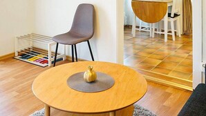 A small dining area with a round wooden table, a grey chair, and a white chair. A small vase is on the table.