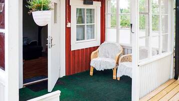 A covered porch with a green carpet, a wicker chair, and a hanging plant.