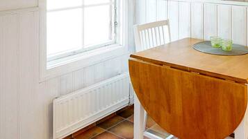 A dining area with a wooden table and chairs, a window with blinds, and a radiator.