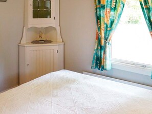 Une chambre à coucher avec un lit, une armoire blanche à porte vitrée et une fenêtre avec des rideaux.