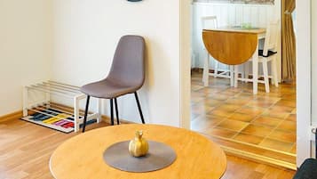 Una habitación con una mesa redonda de madera, una silla gris, un pequeño jarrón decorativo y un zapatero con zapatos de colores.