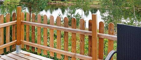 A wooden deck with a view of a lake, surrounded by greenery.