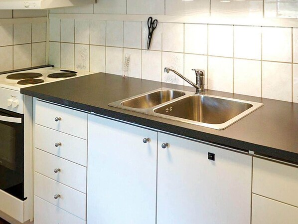 A kitchen with a double sink, a stove, and white cabinets. - 3 Person Holiday Home in Oskarshamn (Oskarshamn)