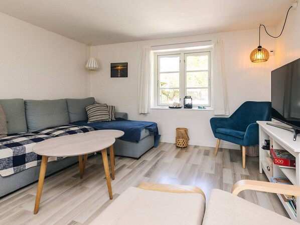 A modern living room with a sofa, a dining table, a TV, and a window with curtains.