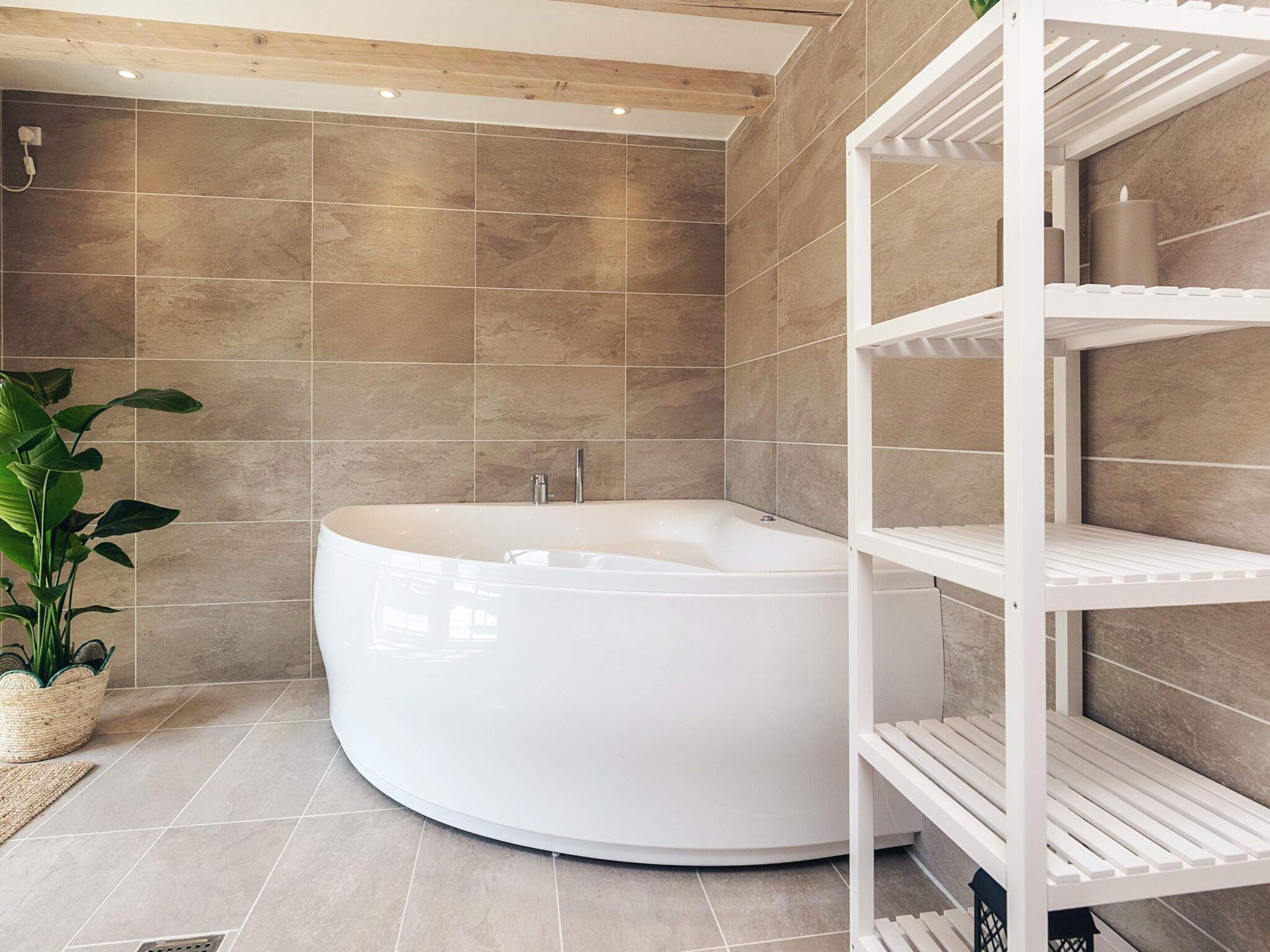 A modern bathroom with a large freestanding bathtub, a white shelving unit, and a potted plant.