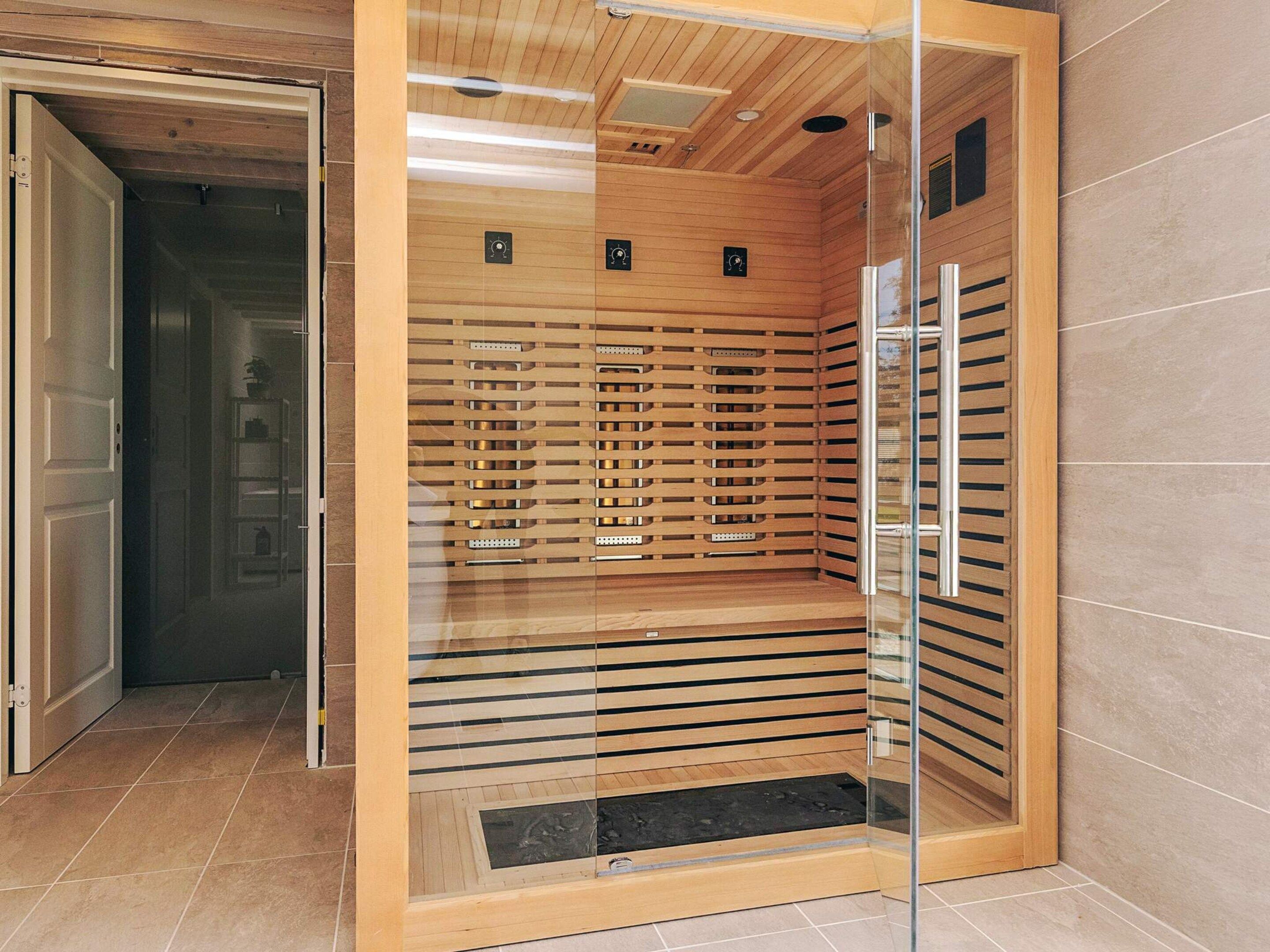 Un ascensor moderno con paneles de madera y puertas de vidrio, que incluye un panel de control con botones y una pantalla digital.