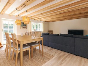 A modern living room with a wooden dining table, chairs, a grey sofa, and a TV.