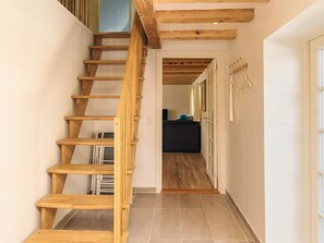 A wooden staircase leading to a room with a tiled floor and a door with a coat rack.