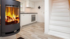 A modern kitchen with a wood-burning stove, white cabinets, and a wooden floor. - 4 Star Holiday Home in Gedser (Gedser)