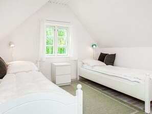 A room with two beds, a window, a bedside table, and a lamp.