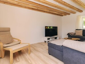 Un salon moderne avec un plafond en bois, un téléviseur, un canapé et un fauteuil.