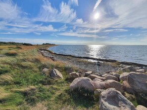 A coastal landscape with a rocky shoreline, grassy areas, and a clear sky. - 4 Star Holiday Home in Gedser (Gedser)