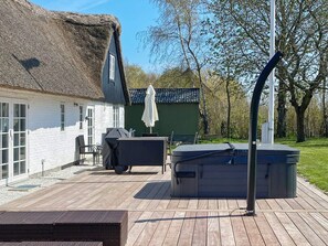 A wooden deck with a hot tub, a grill, and a thatched-roof building. - 4 Star Holiday Home in Gedser (Gedser)