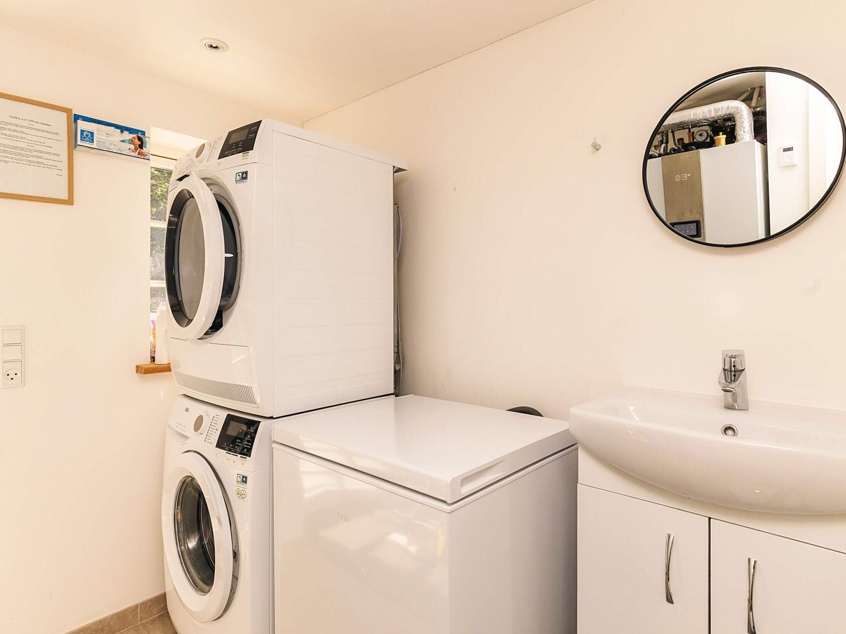 A compact laundry room with a front-loading washer and dryer, a sink, and a mirror.
