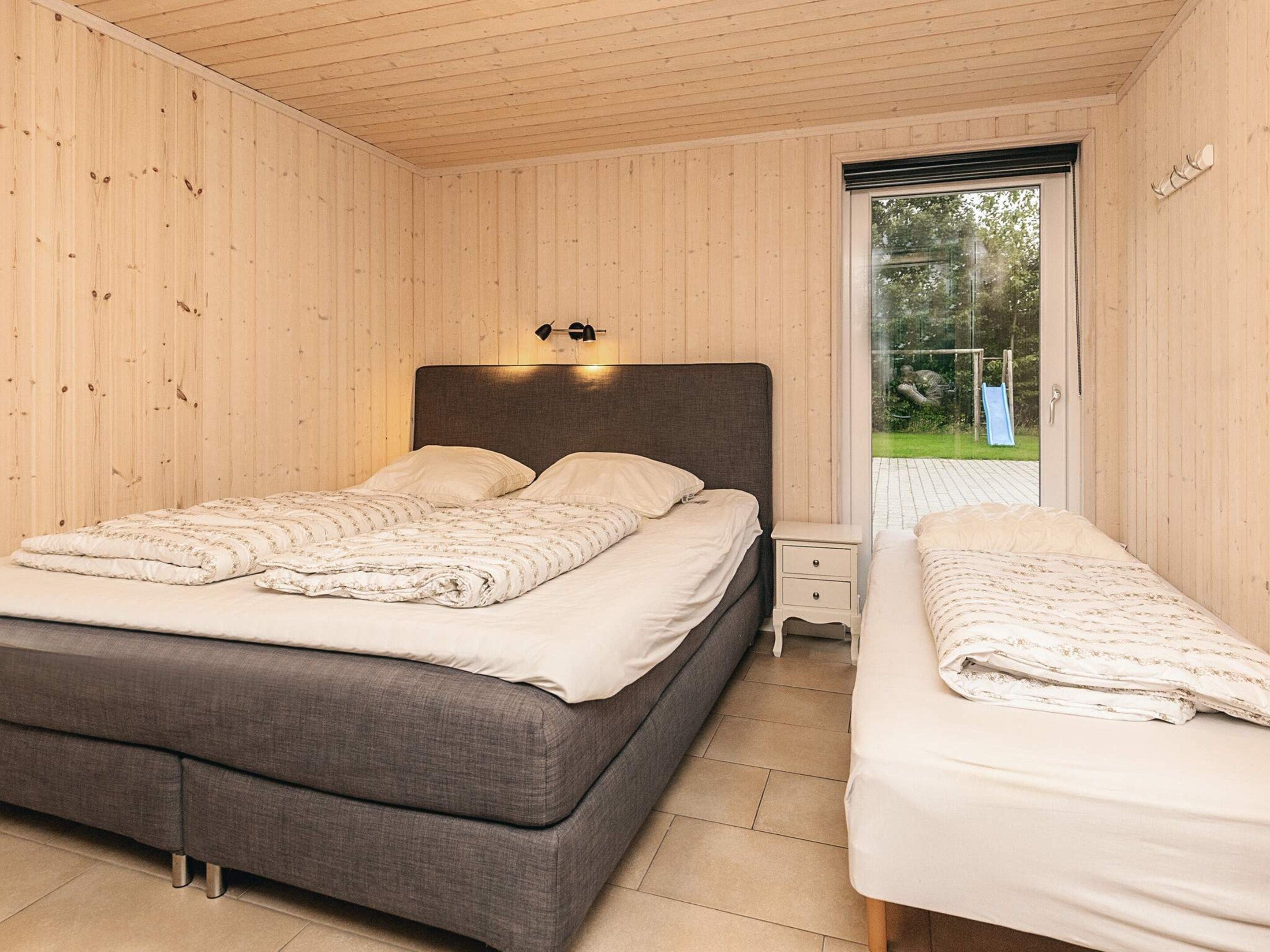 A bedroom with a large bed, a smaller bed, a nightstand, and a window with a view of the outdoors.