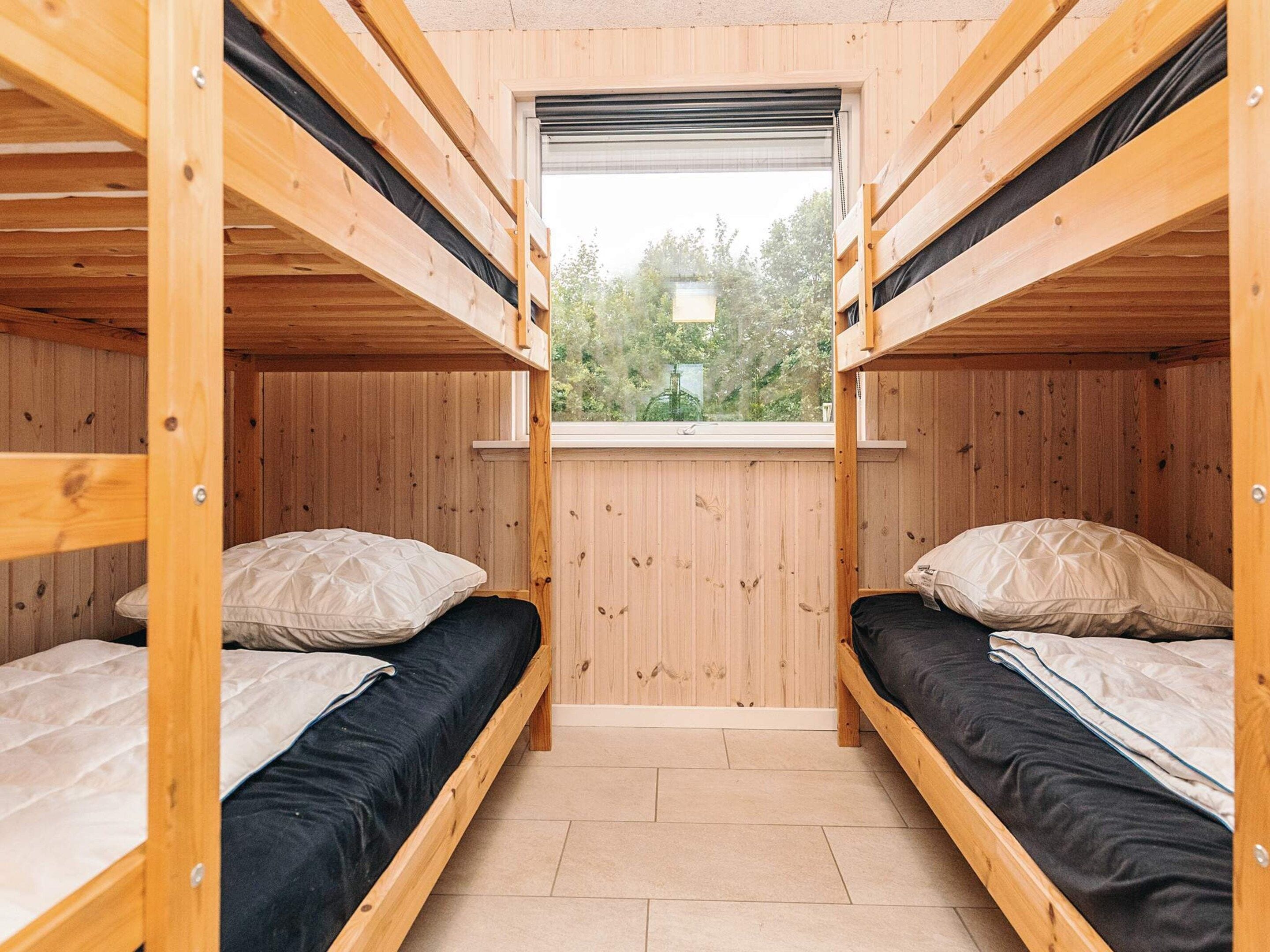 Habitación pequeña con dos literas, paredes de madera, un ventanal y suelo de baldosas.