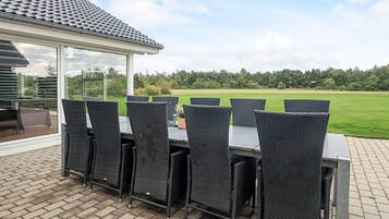An outdoor patio with a table and chairs, a glass enclosure, and a view of a green field.
